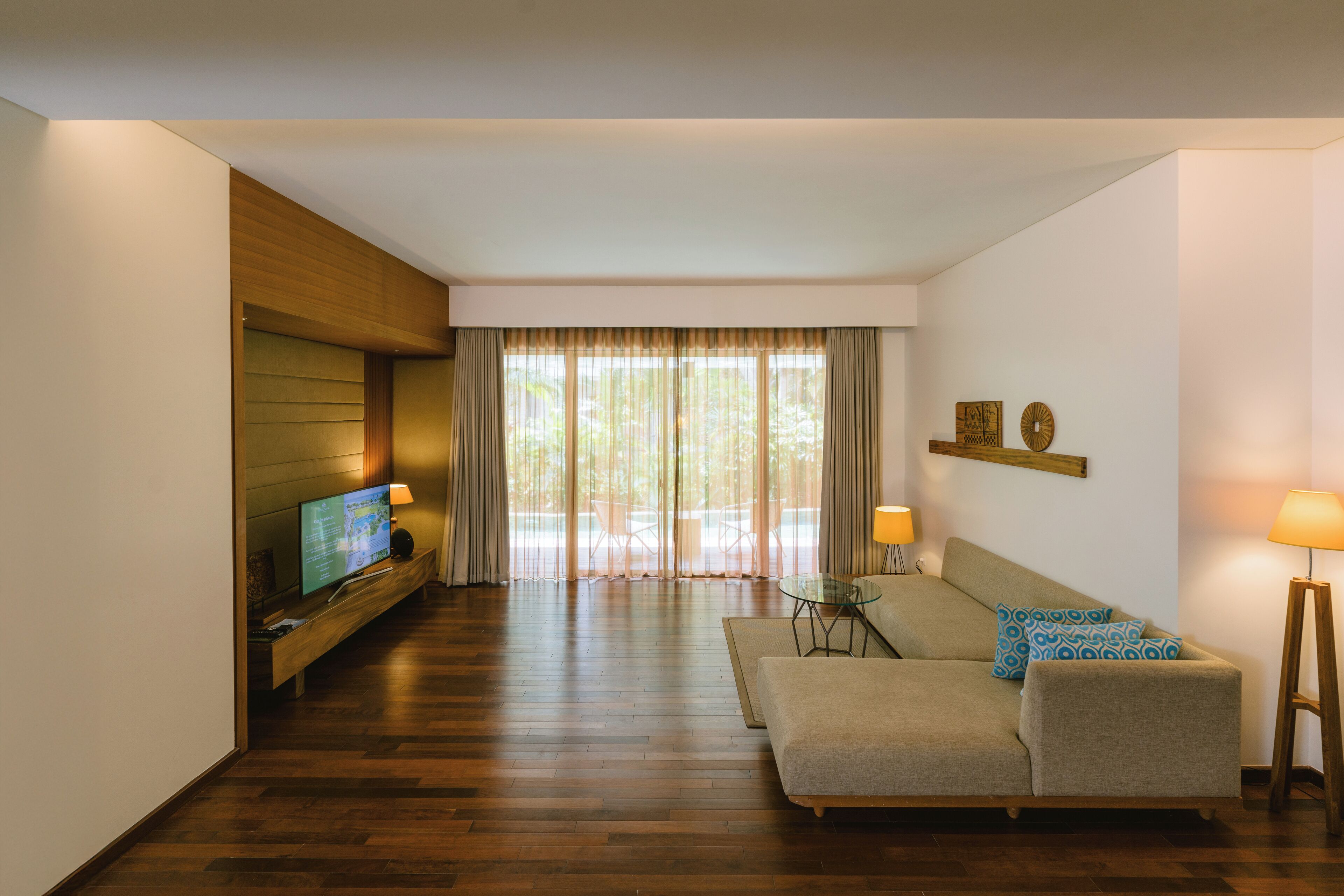 Una sala de estar moderna con suelo de madera, un sofá, un televisor y una mesa de vidrio.