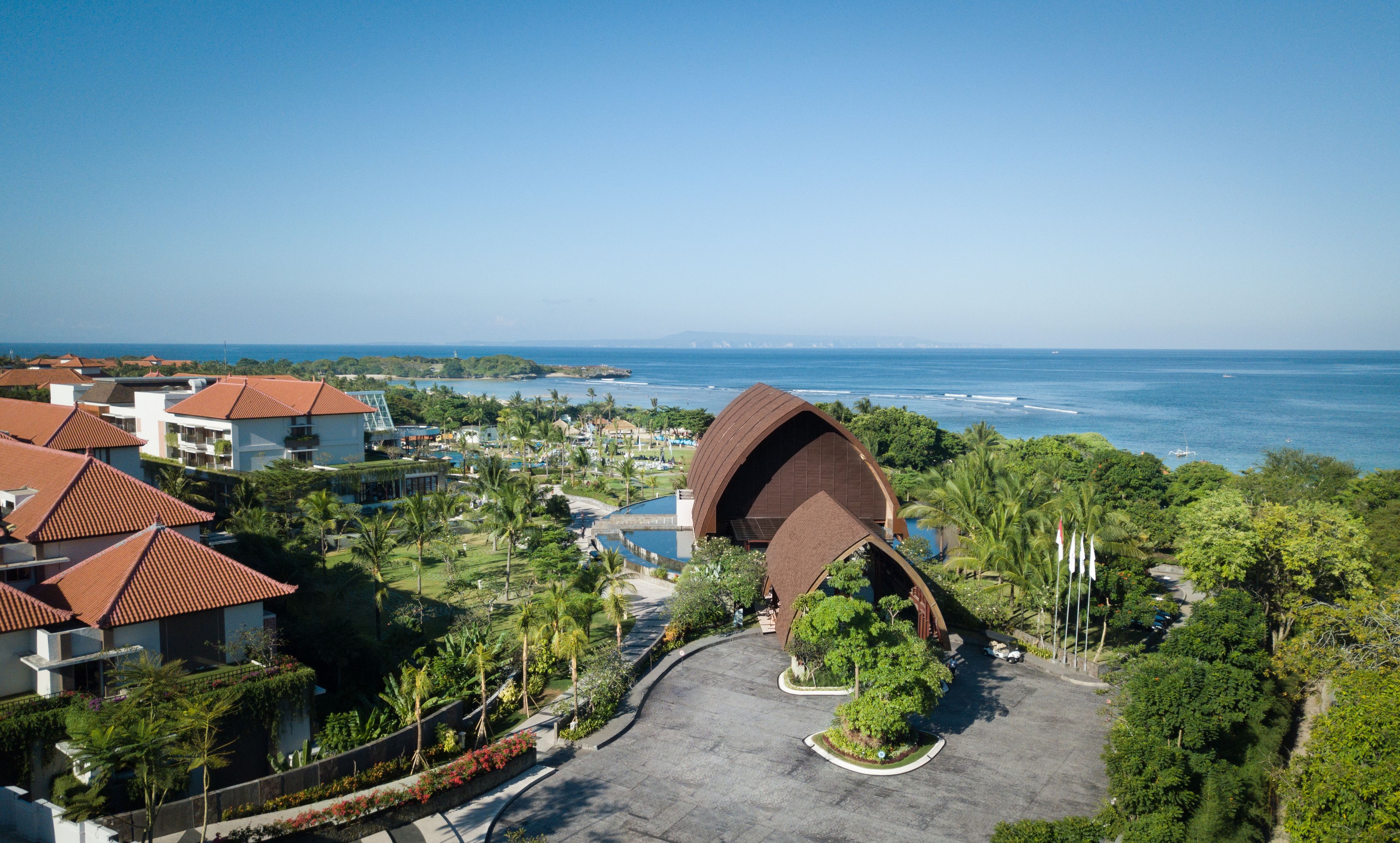 A resort with a distinctive curved building, a pool, and a view of the ocean.
