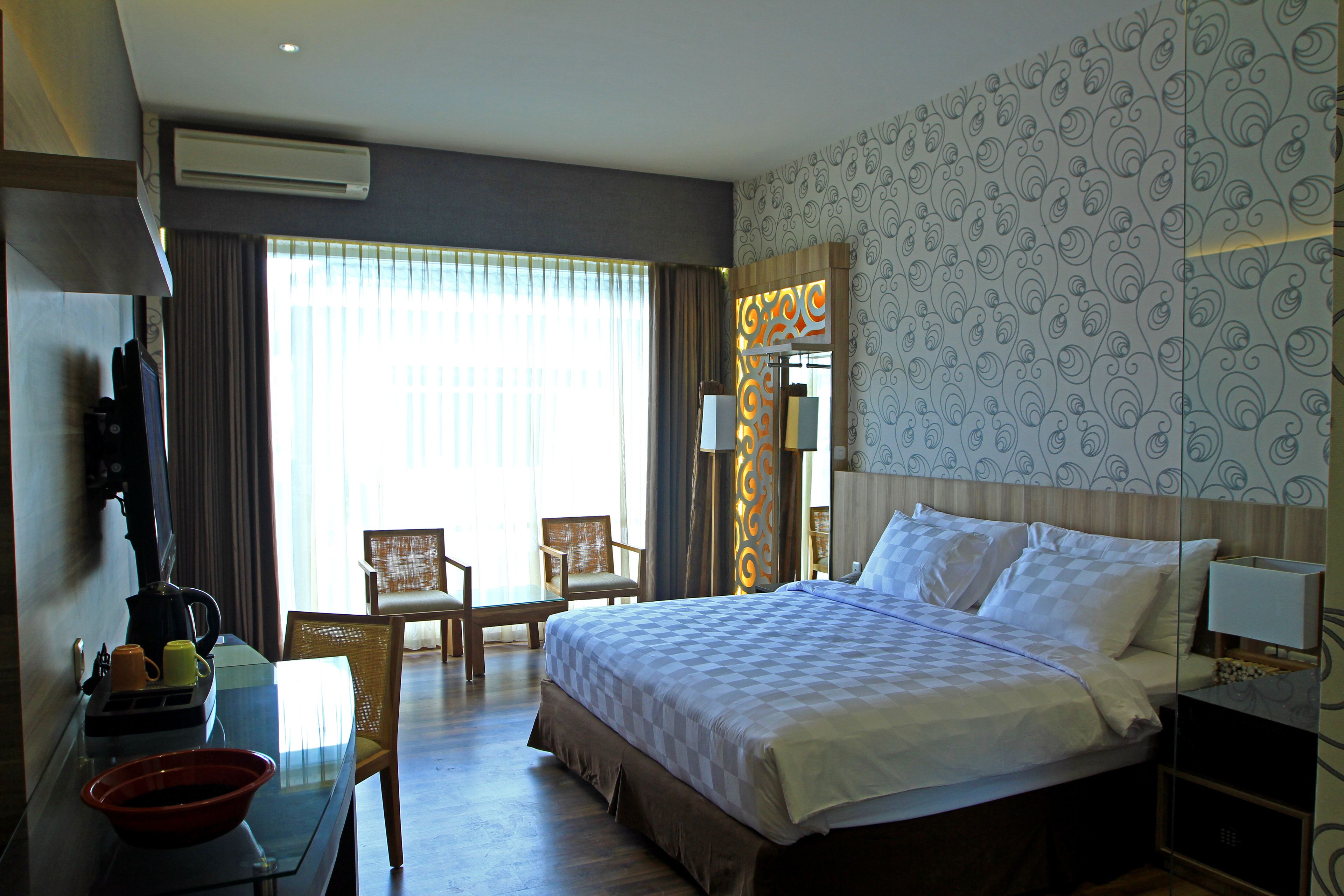 A hotel room with a large bed, two chairs, a desk with a coffee maker, and a bowl.