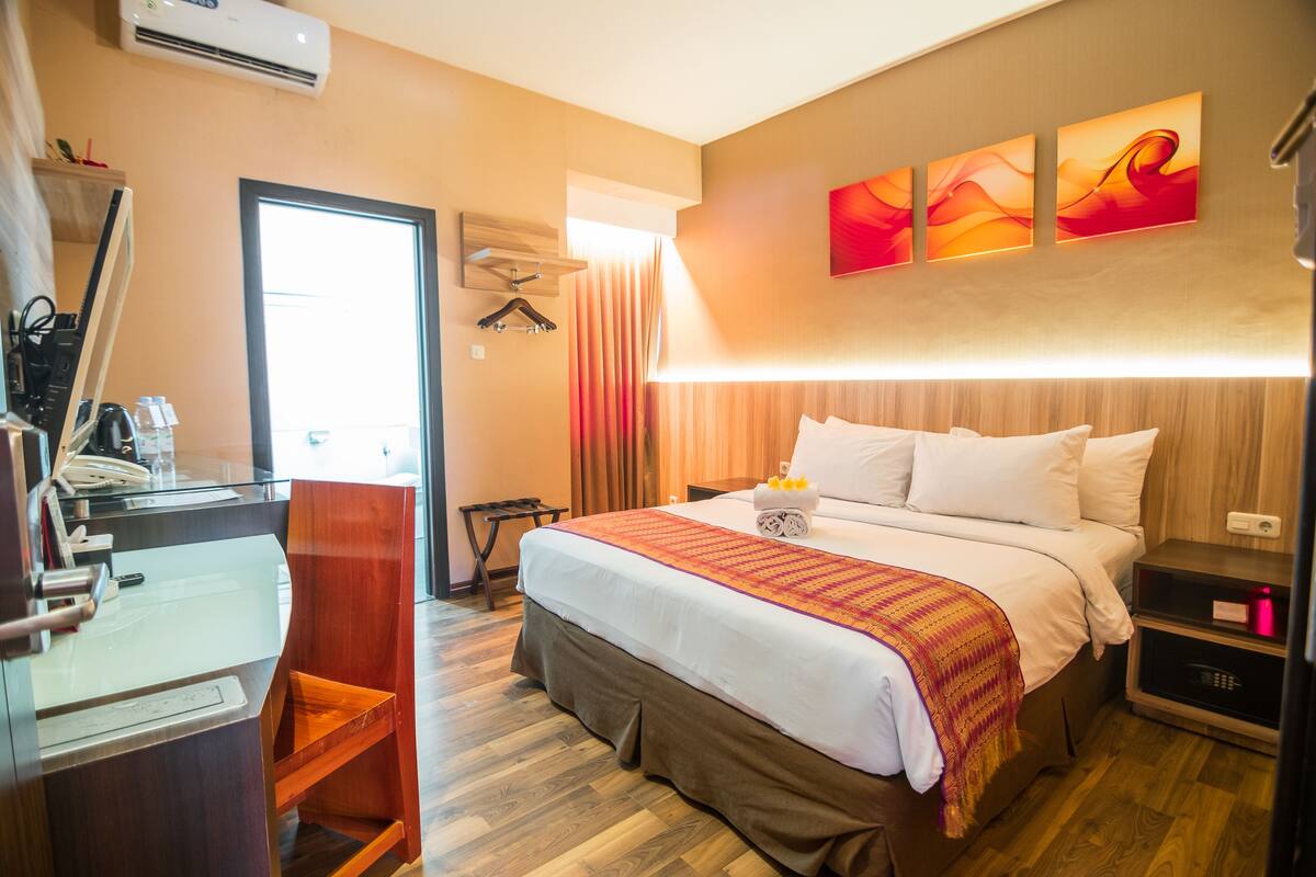 A hotel room with a bed, a desk, a chair, a desk lamp, and a wall-mounted air conditioner.