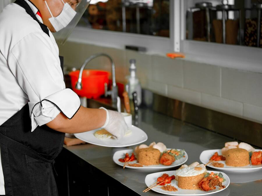 A chef preparing food in a kitchen with stainless steel counters and a window in the background.
