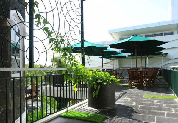 An outdoor patio area with a stone floor, green umbrellas, and a potted plant. - Ox Ville Hotel (Padang)