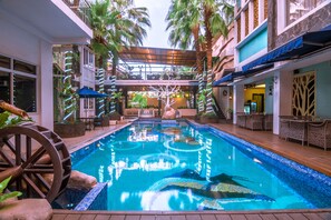 A swimming pool with a wooden deck, surrounded by lounge chairs and potted plants. - Ox Ville Hotel (Padang)