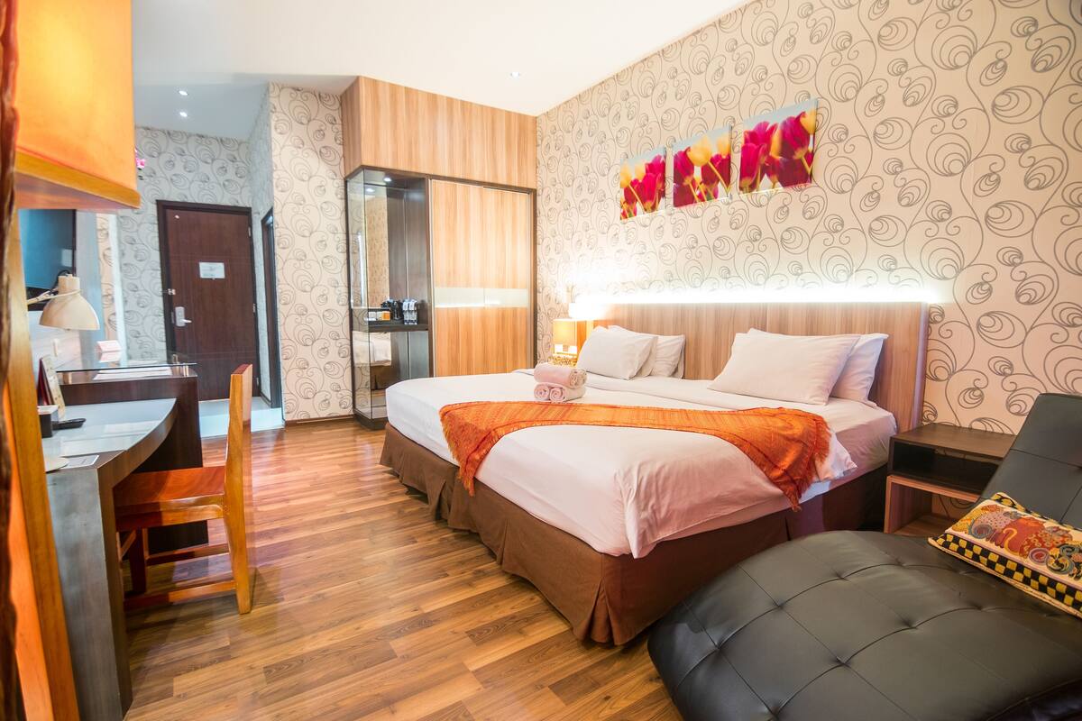 A hotel room with a large bed, a desk with a chair, a small table, and a sofa.
