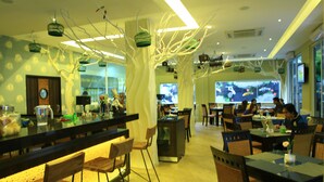 Un restaurante con una decoración moderna, que presenta una zona de bar con taburetes y mesas, elementos decorativos colgantes y vistas de la ciudad a través de amplios ventanales.