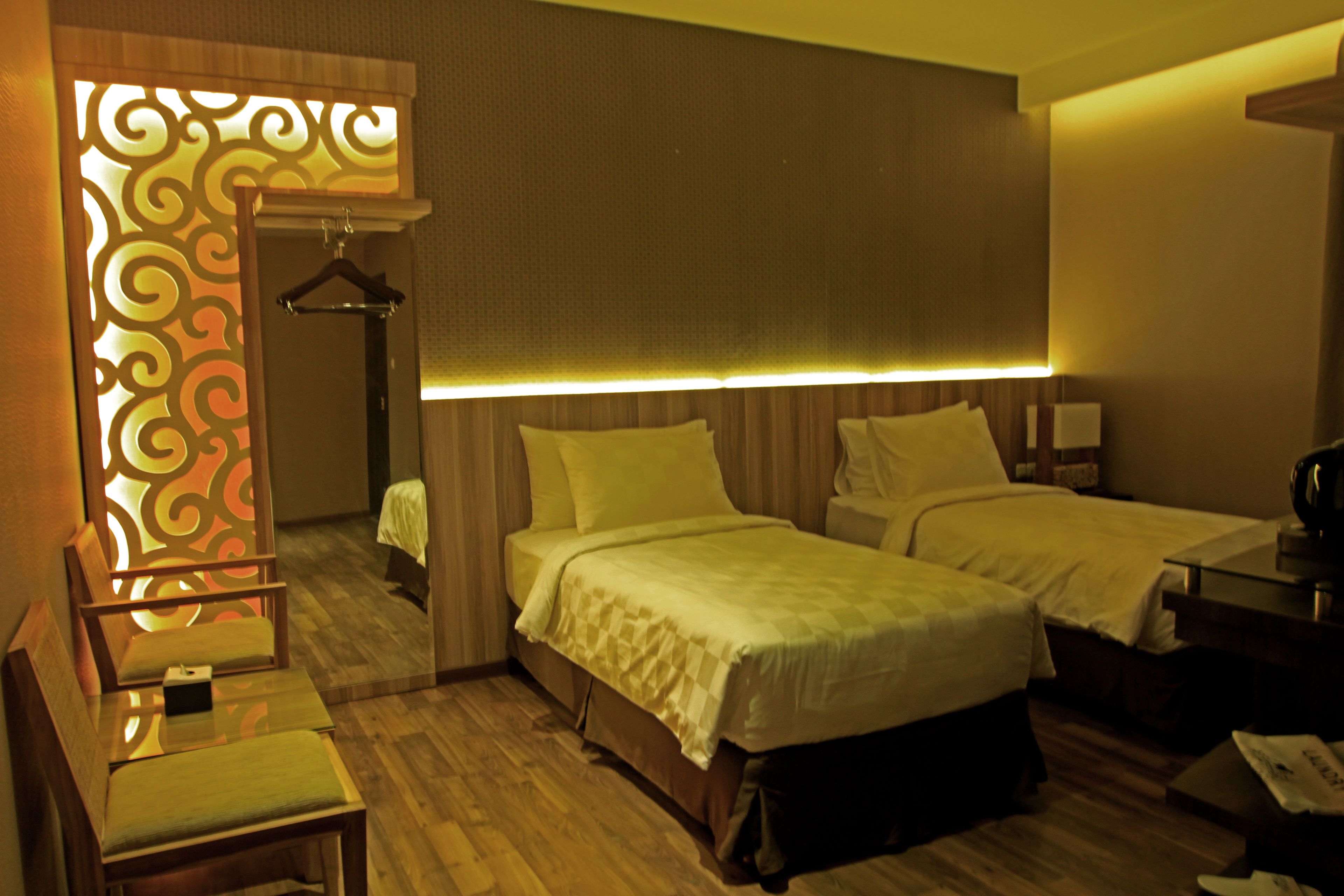 A hotel room with two beds, a desk, a chair, and a decorative partition.