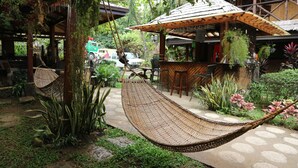Una hamaca en un jardín con un porche de madera, un bar y diversas plantas.