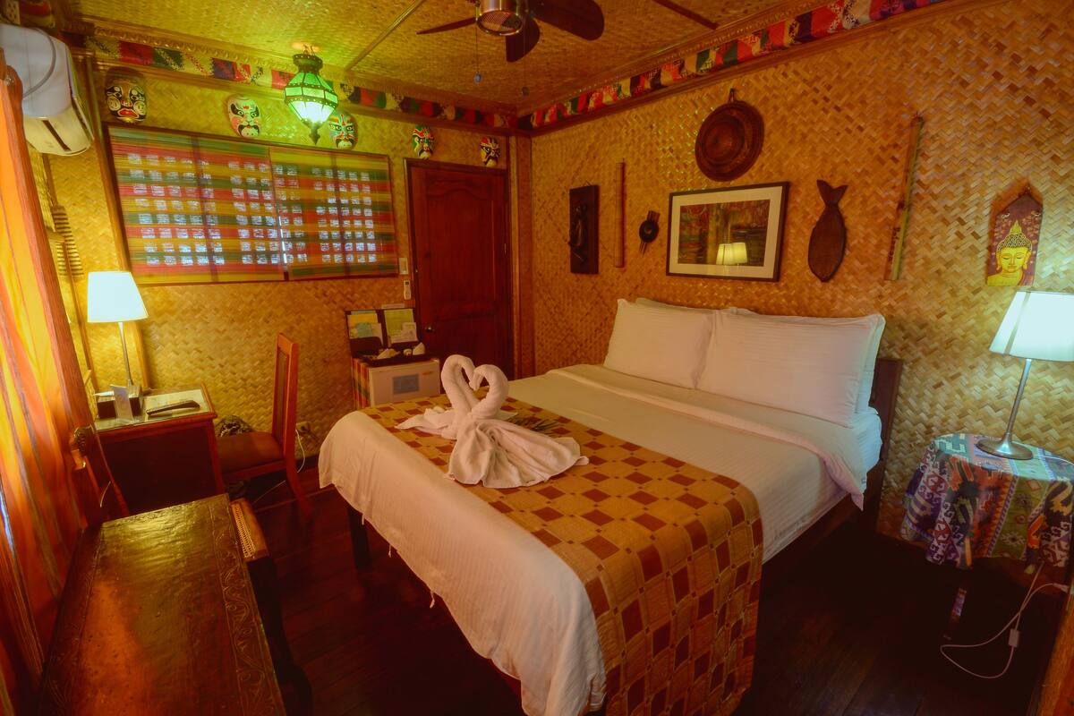 A hotel room with a bed, a desk, a chair, a lamp, and a wall with decorative items.