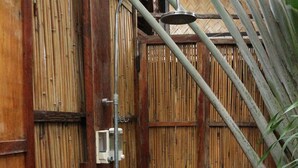Puerta de bambú con cabezal de ducha metálico y una pequeña estantería.