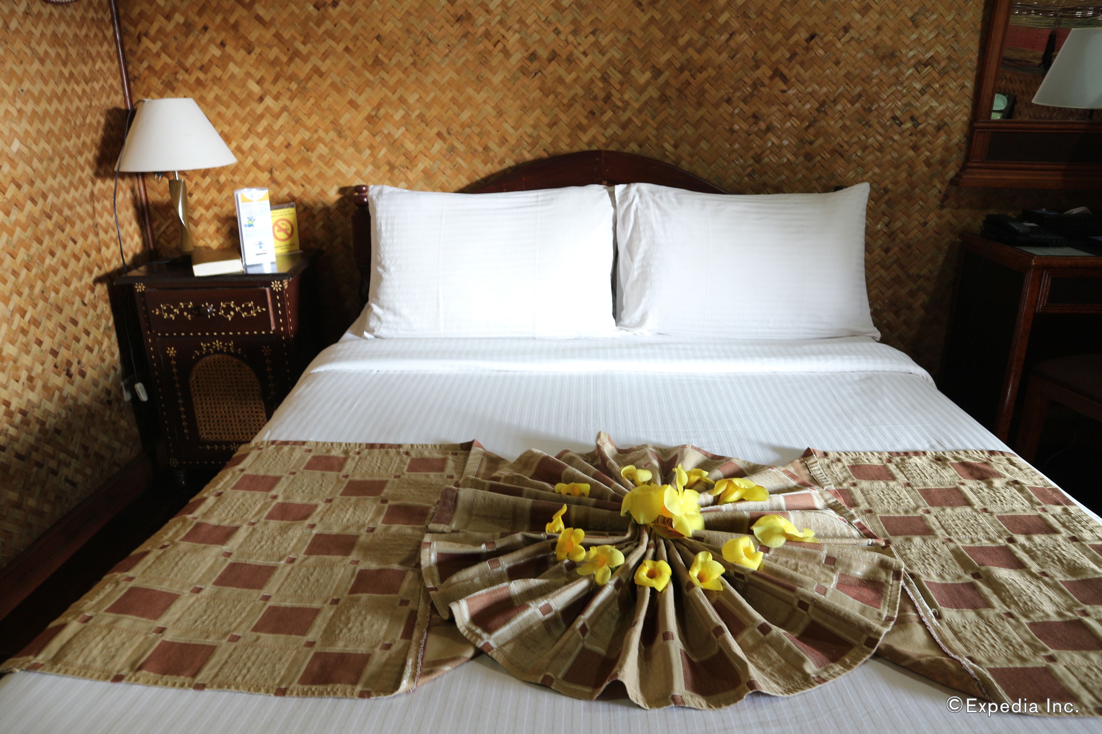 Een hotelkamer met een bed, een nachtkastje met een lamp en een decoratieve bloemstelling op het bed.