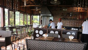 Un restaurante con mobiliario de mimbre, una zona de bar y amplios ventanales.