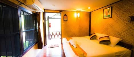 Habitación de hotel con una cama grande, una ventana con rejas, piso de madera y aire acondicionado de pared.