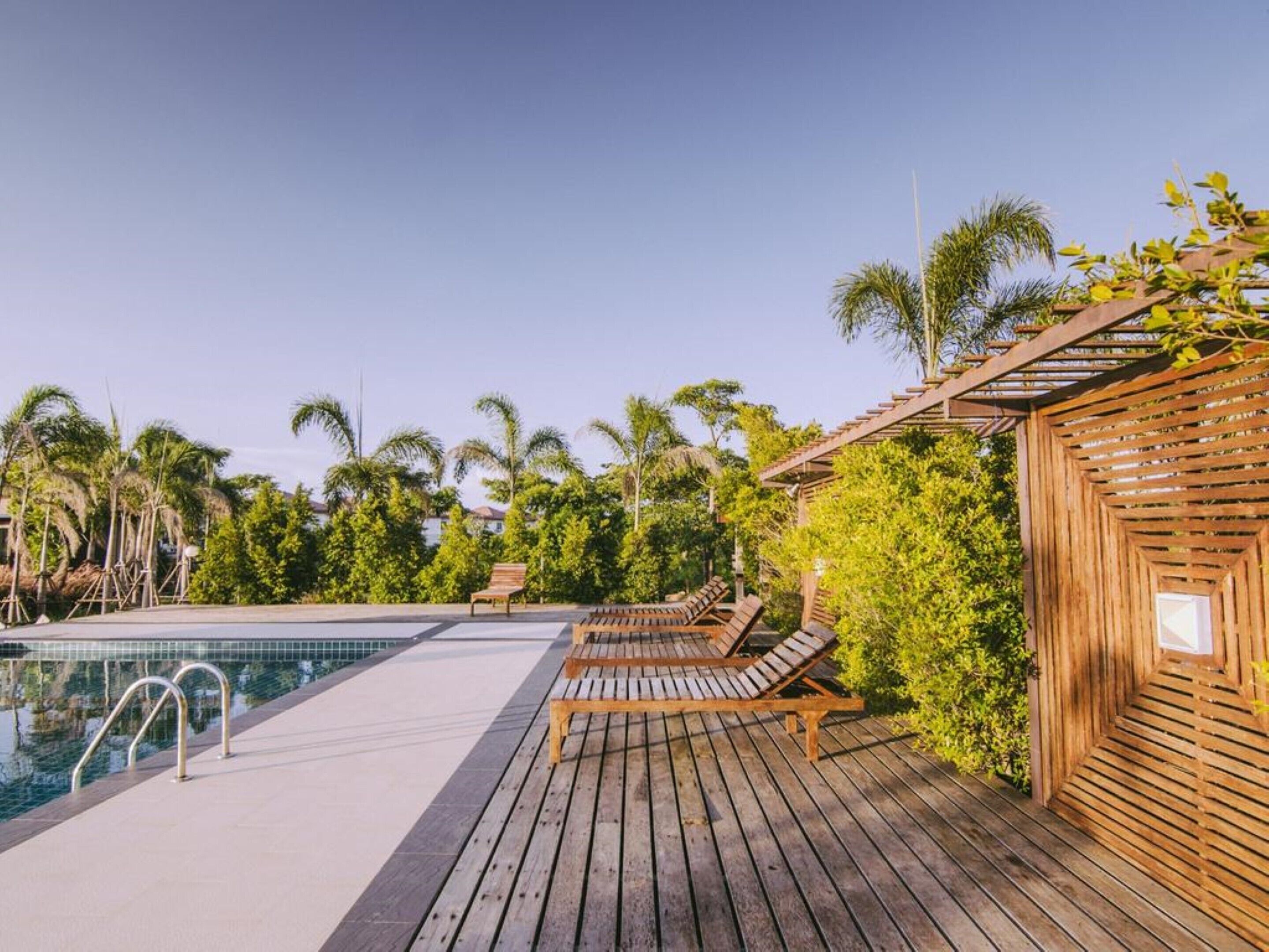 A wooden deck with a pool, lounge chairs, and a wooden pergola.