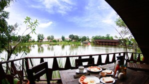 Una mesa de madera con alimentos para el desayuno y vistas a un lago tranquilo y edificios al fondo.