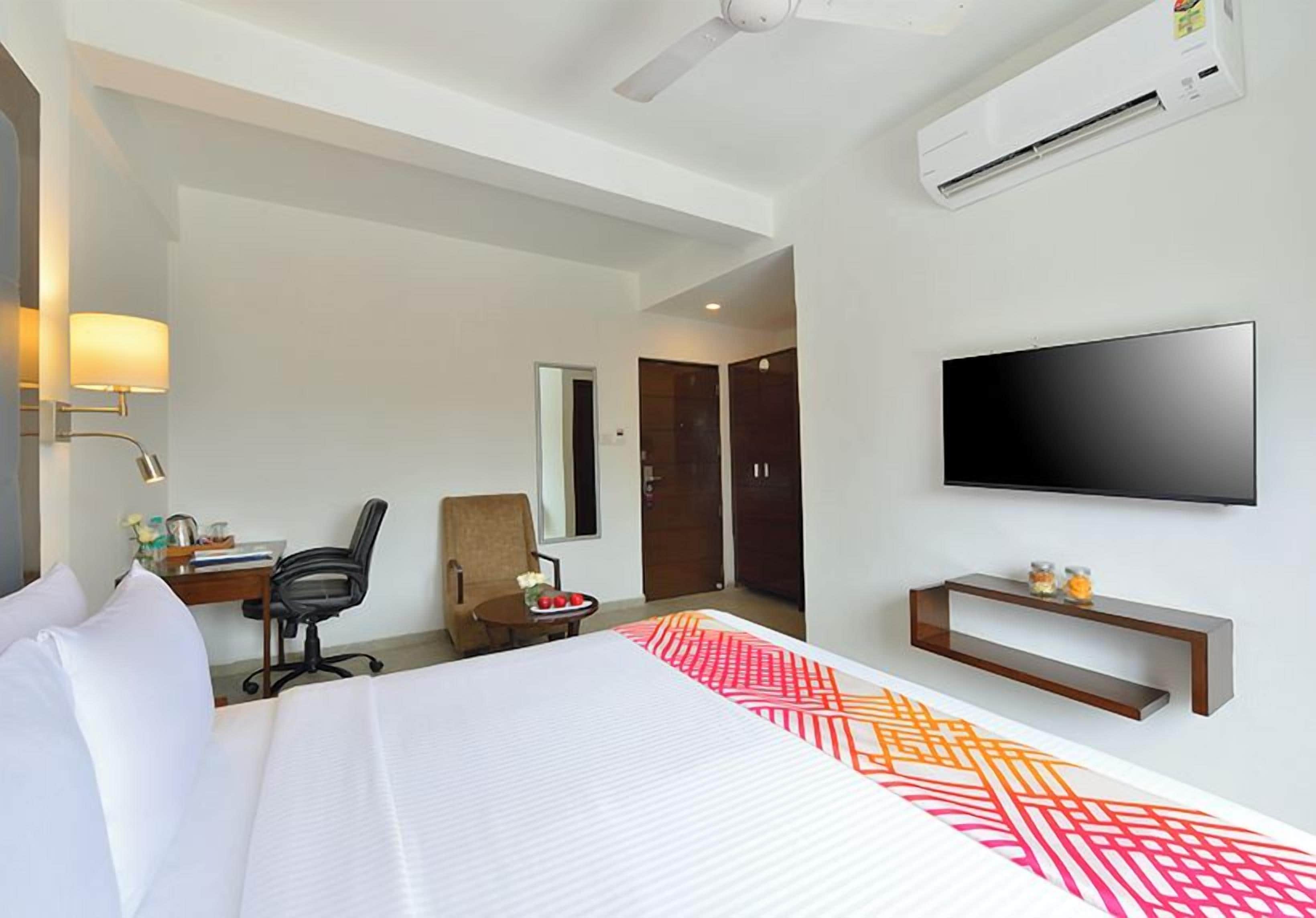 Quarto de hotel com cama, escrivaninha, cadeira, televisão e ar condicionado.