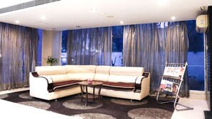 A modern living room with a beige sectional sofa, a small round table, and a magazine rack. - Hotel Clarks Collection Bhavnagar (Bhavnagar)