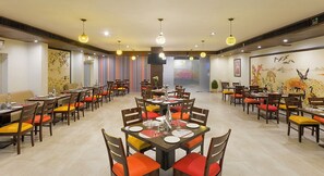 A restaurant with multiple tables and chairs, some with orange cushions. - Ginger Bhavnagar, Kalubha Road (Bhavnagar)