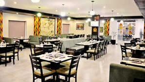 A restaurant with multiple dining tables and booths, equipped with chairs and table settings. - Hotel Clarks Collection Bhavnagar (Bhavnagar)