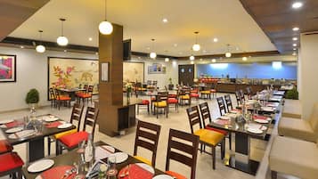 Un restaurante con varias mesas y sillas, una zona de mostrador y obras de arte en las paredes.