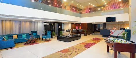 A spacious lobby with a high ceiling, a reception desk, seating area, and a foosball table.