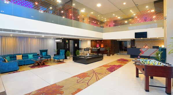 A spacious lobby with a high ceiling, a reception desk, seating area, and a foosball table.