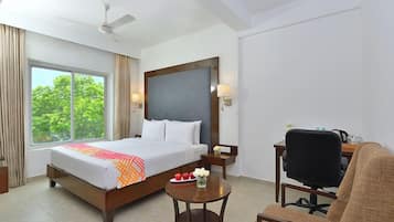 Una habitación de hotel con cama, escritorio, silla, mesita y ventilador de techo.
