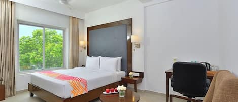 Una habitación de hotel con cama, escritorio, silla, mesita y ventilador de techo.