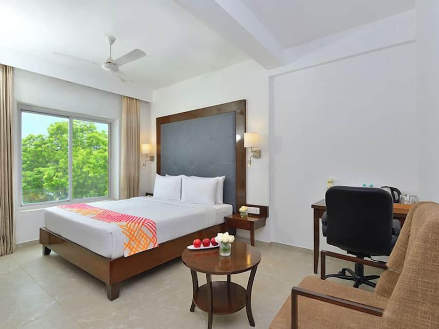 A hotel room with a bed, a desk, a chair, a small table, and a ceiling fan.