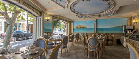 A restaurant with outdoor seating, a mural of a coastal scene, and a view of the street.