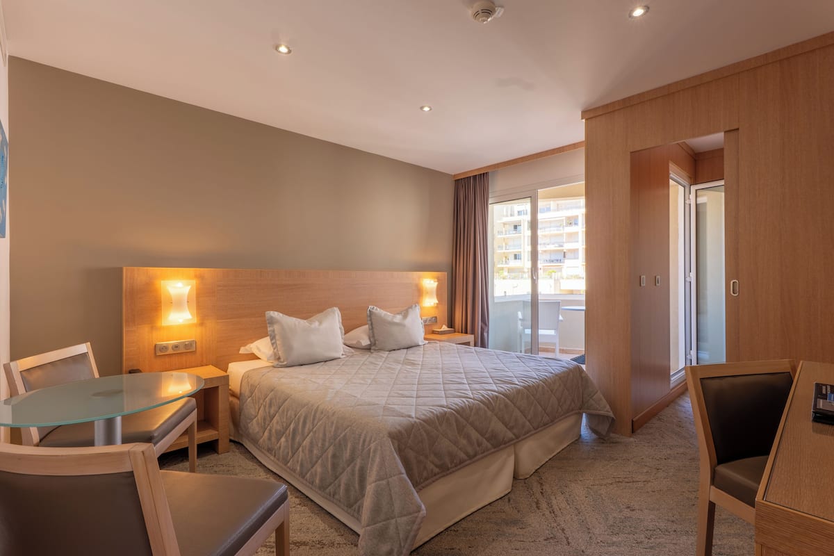 Una habitación de hotel con cama, una mesita de vidrio, una silla, una mesita de noche y un armario.