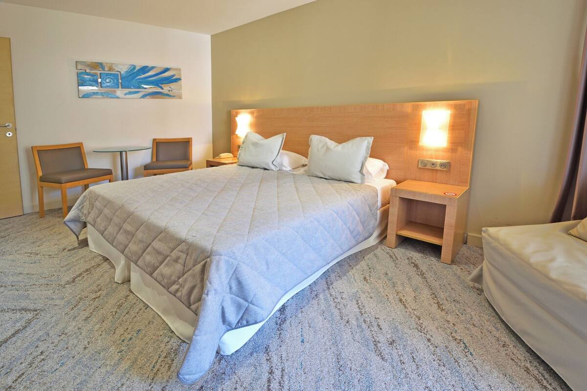 Una habitación de hotel con una cama grande, dos mesitas de noche, una pequeña mesa, dos sillas y una obra de arte en la pared.