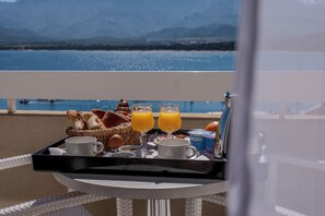 A breakfast tray with bread, eggs, juice, and a box of cereal on a balcony overlooking a body of water and mountains.