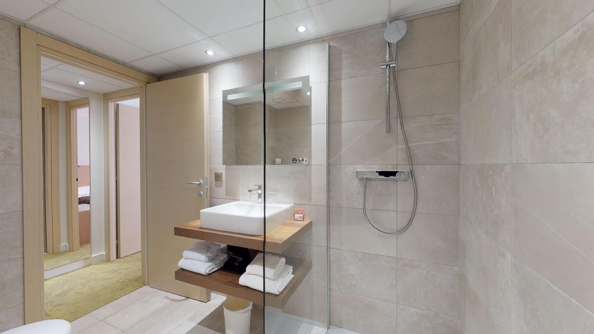 A modern bathroom with a glass-enclosed shower, a wooden vanity, and a mirror above the sink.