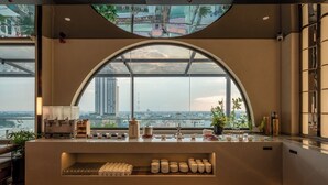 A modern bar area with a large arched window, a counter with various items, and a view of a cityscape. - The IRIS Signature Hotel & Spa (Can Tho)