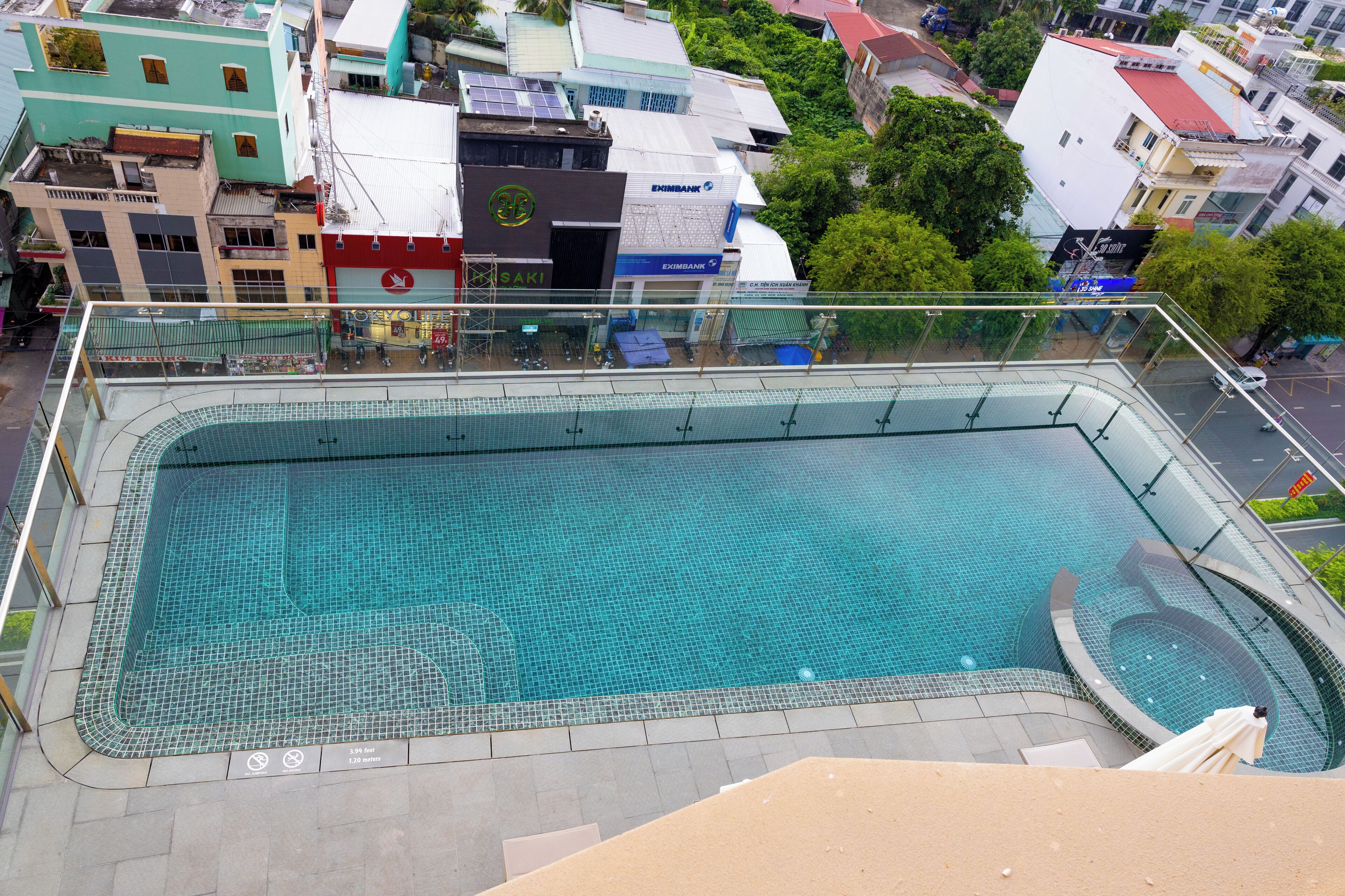 A rooftop swimming pool with a glass barrier, surrounded by urban buildings.
