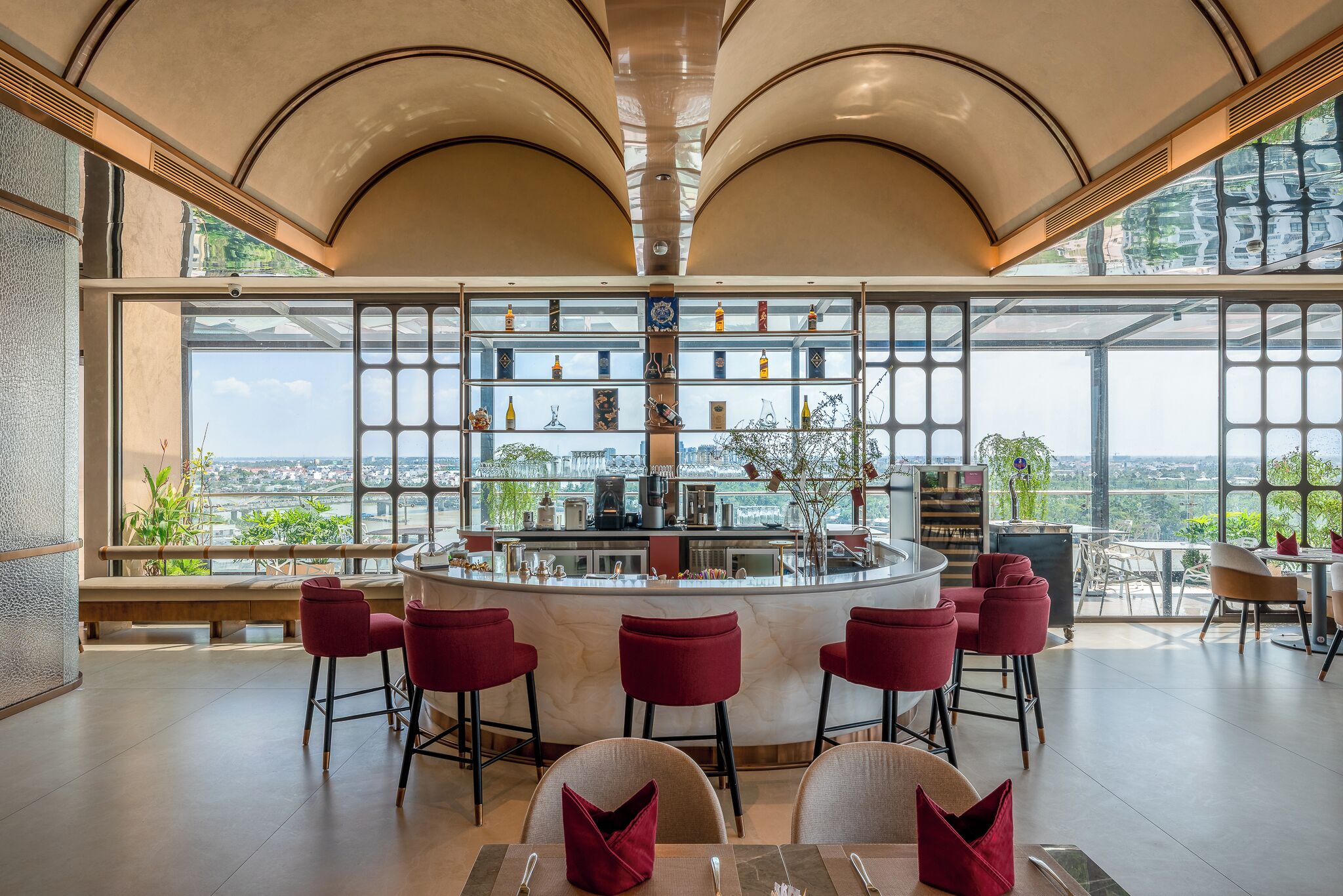 A bar area with a view of the city, red bar stools, and a high ceiling.