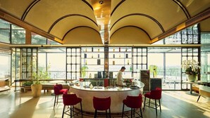 A modern bar area with a central counter, red bar stools, and a view through large windows. - The IRIS Signature Hotel & Spa (Can Tho)