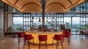 A modern bar area with a curved counter, red bar stools, and a large window offering a city view. - The IRIS Signature Hotel & Spa (Can Tho)