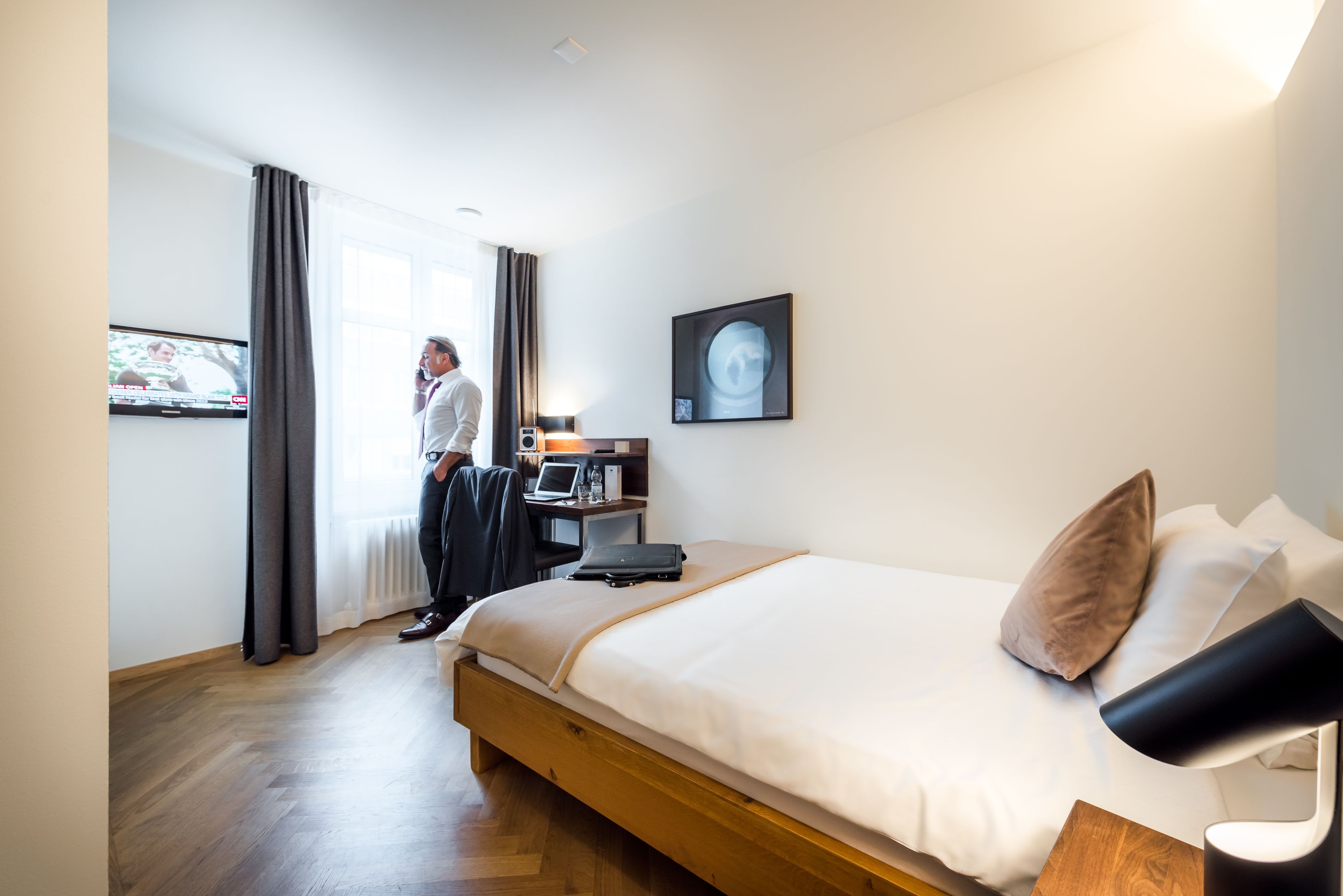 Une chambre d’hôtel avec un lit, un bureau avec un ordinateur, une télévision et une fenêtre avec des rideaux.
