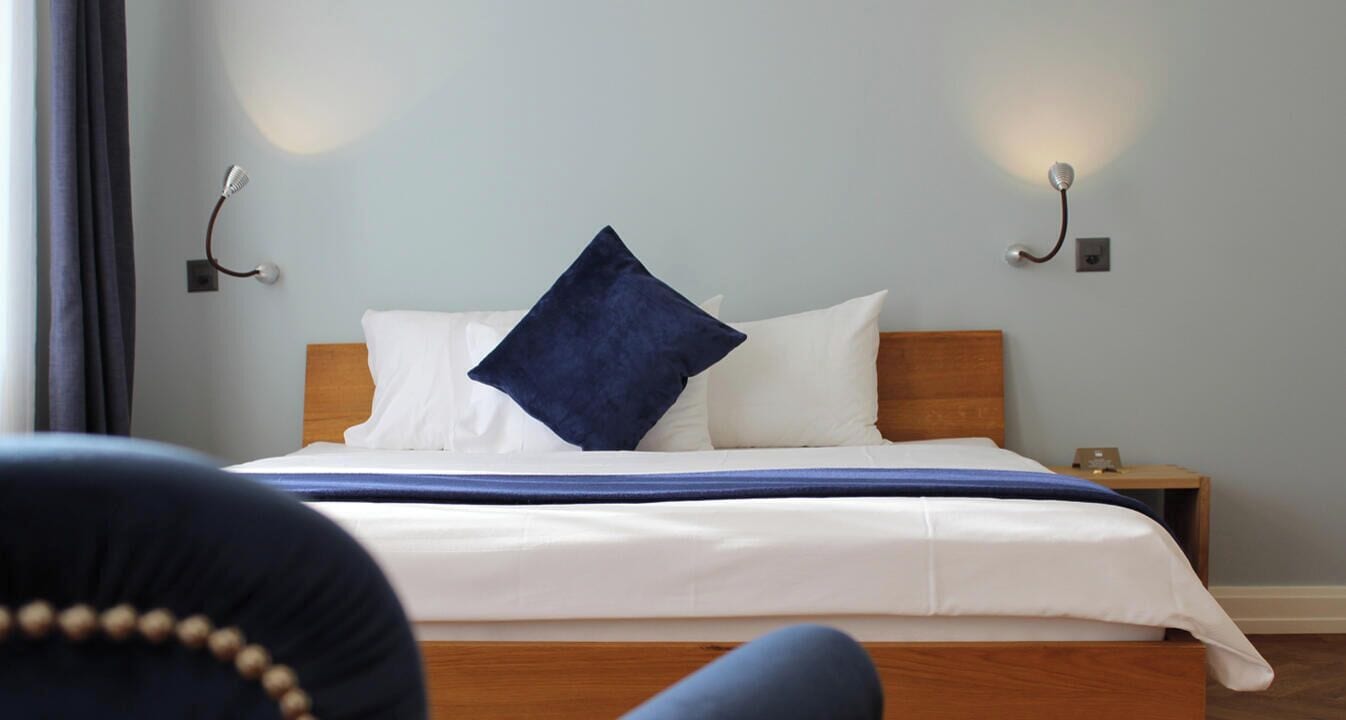 A neatly made bed with white and blue bedding, a wooden headboard, and two bedside lamps.
