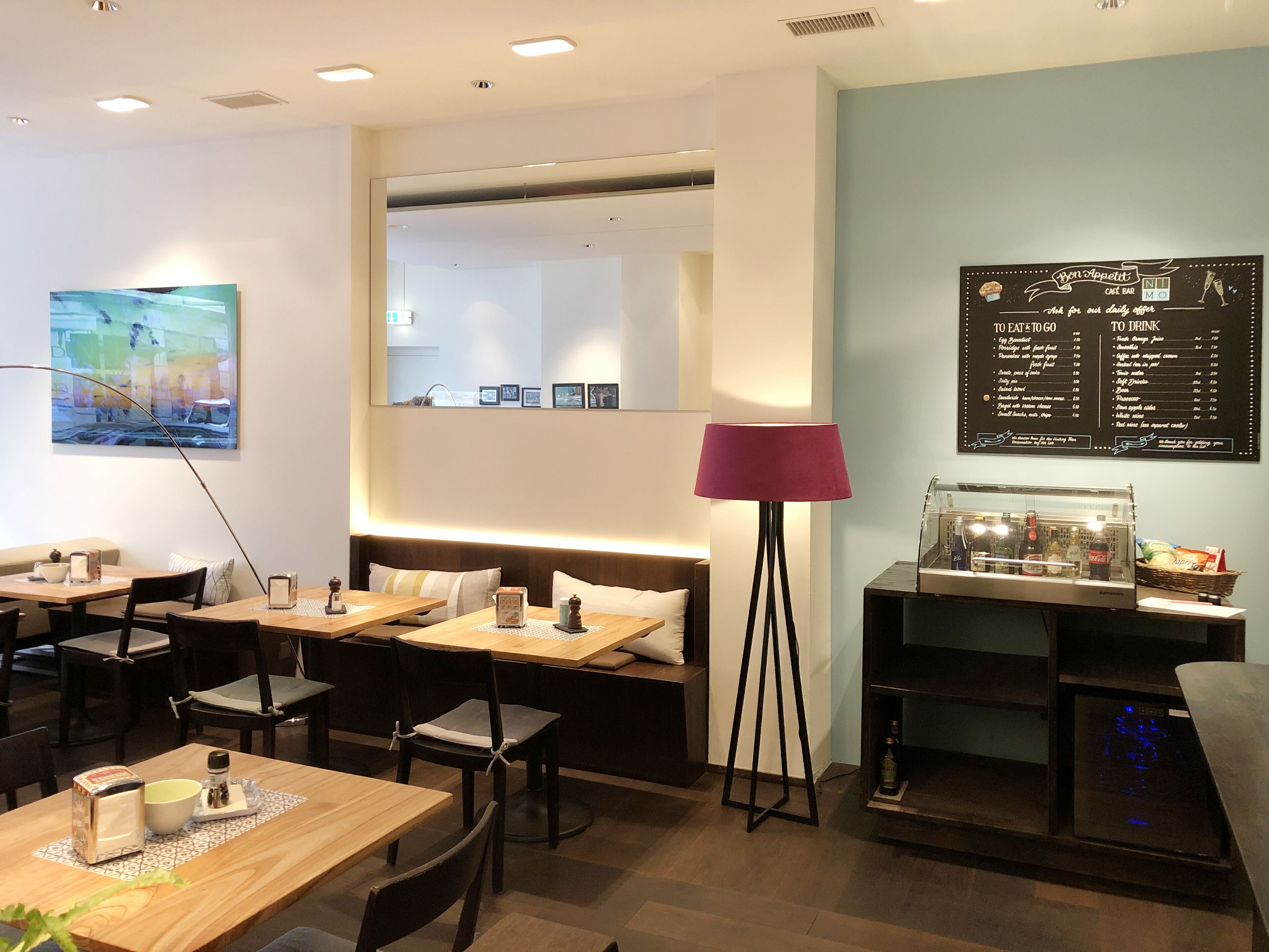 A cafe with wooden tables and chairs, a sofa, a lamp, and a menu board.
