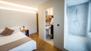 Una habitación de hotel moderna con una cama, una mesita de noche, un baño con ducha y una cocina visible.