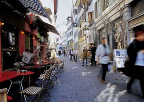 A cobblestone street with outdoor seating and a restaurant. - Boutique Hotel NI-MO (Zürich)