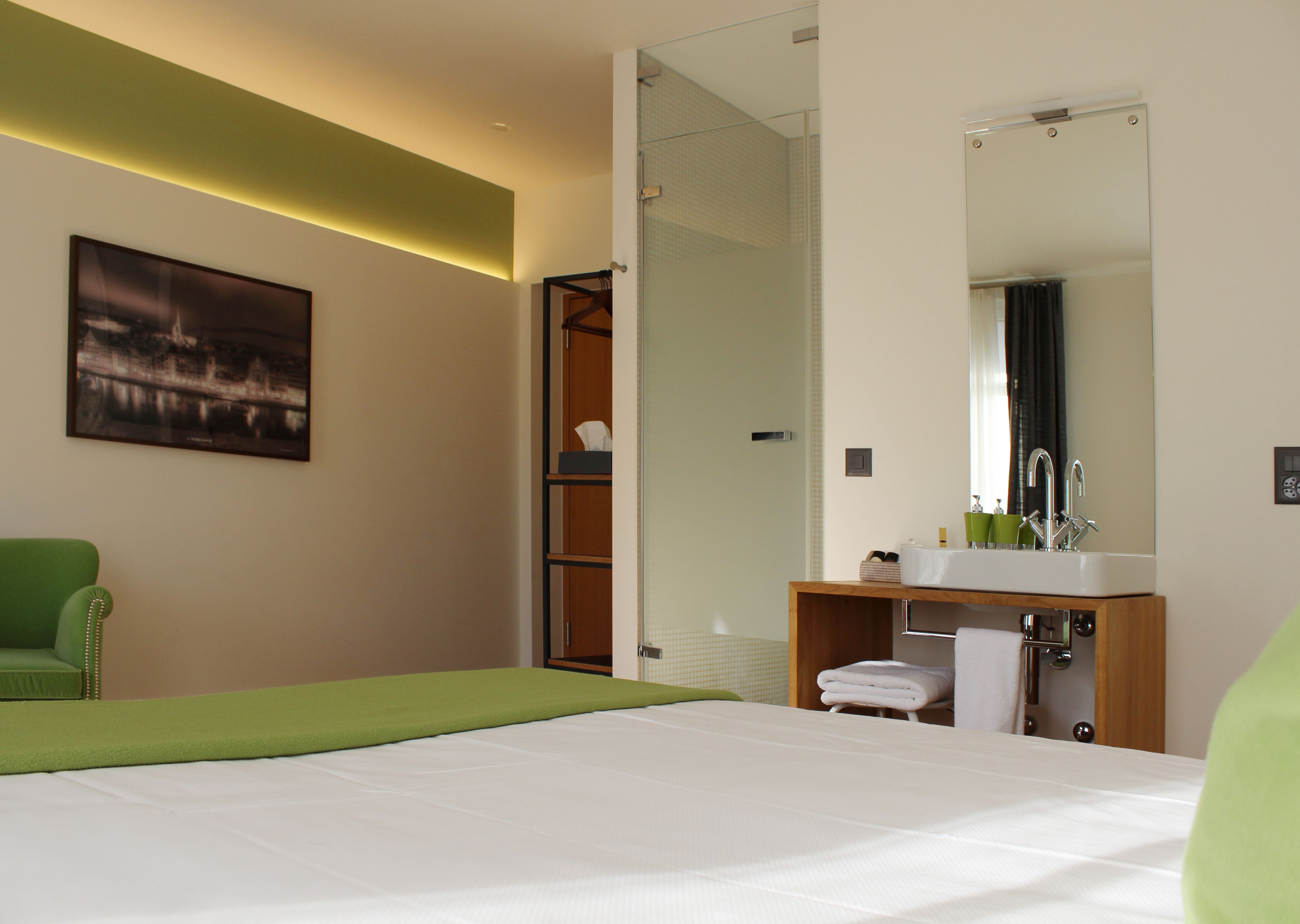Habitació d'hotel amb un llit, una cadira verda, un armari de fusta amb un mirall i una zona de banyera.