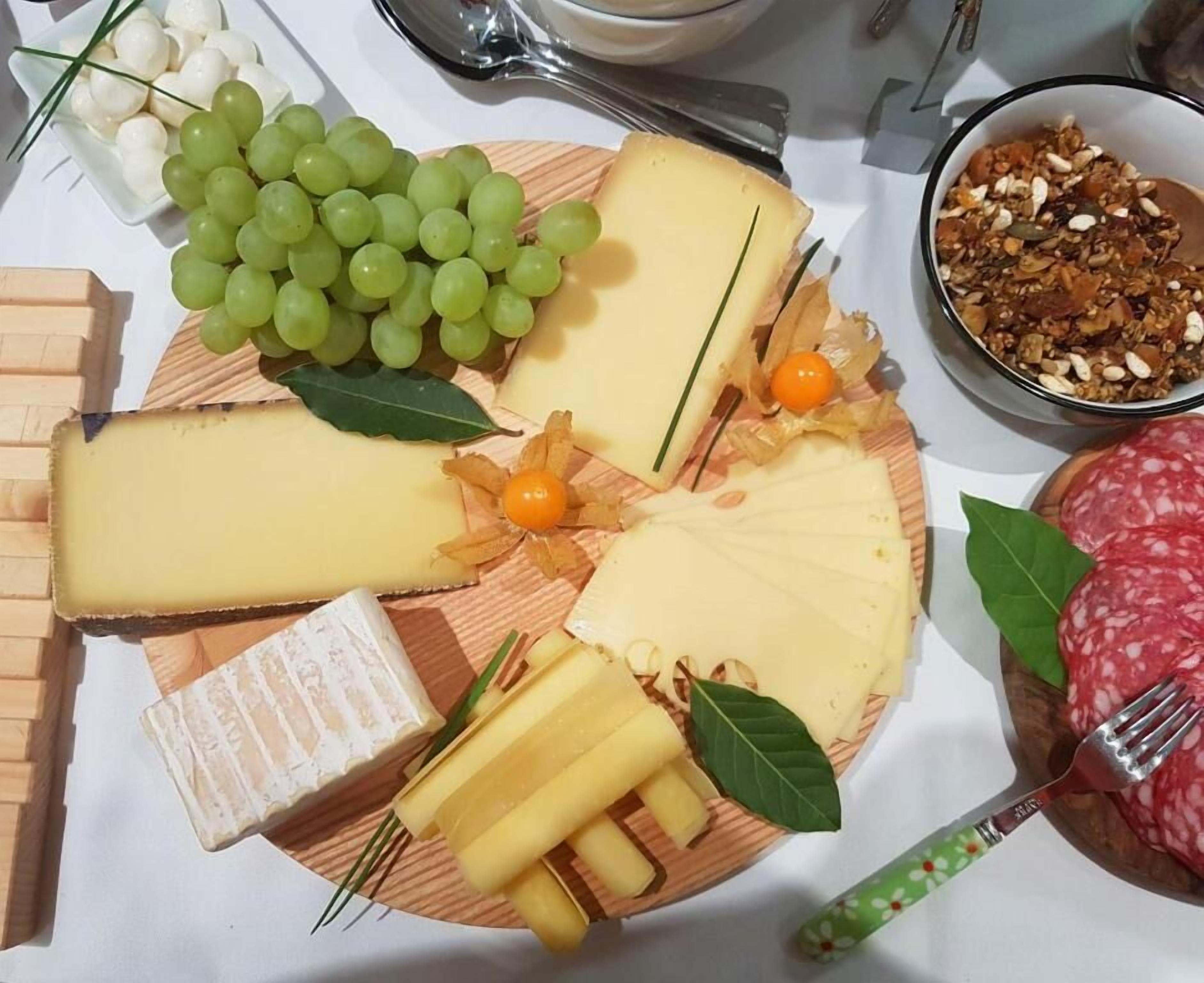 Un plateau de fromages comprenant différents types de fromages, des raisins et un bol de noix.