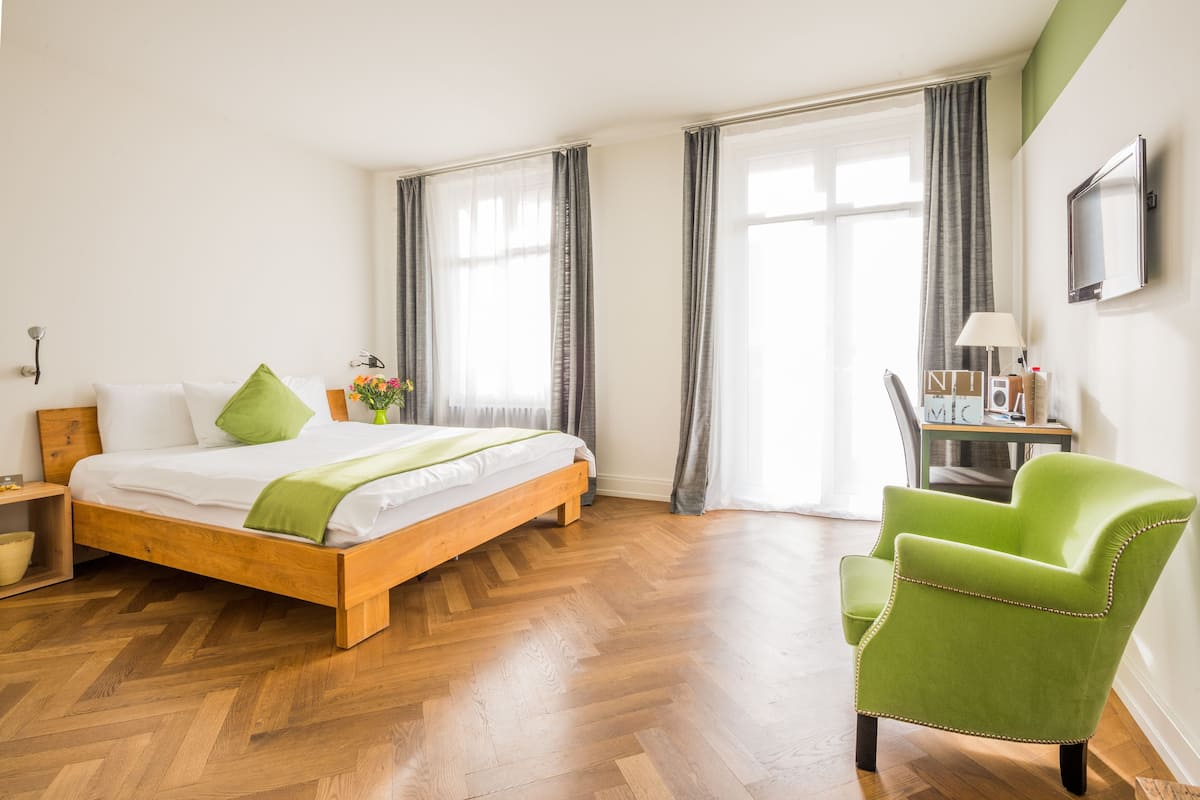 A bedroom with a wooden bed, green pillows, a green chair, a bedside table, and a window with curtains.