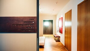Un pasillo con suelo de madera, un banco y una puerta. Hay un cartel en la pared con texto.