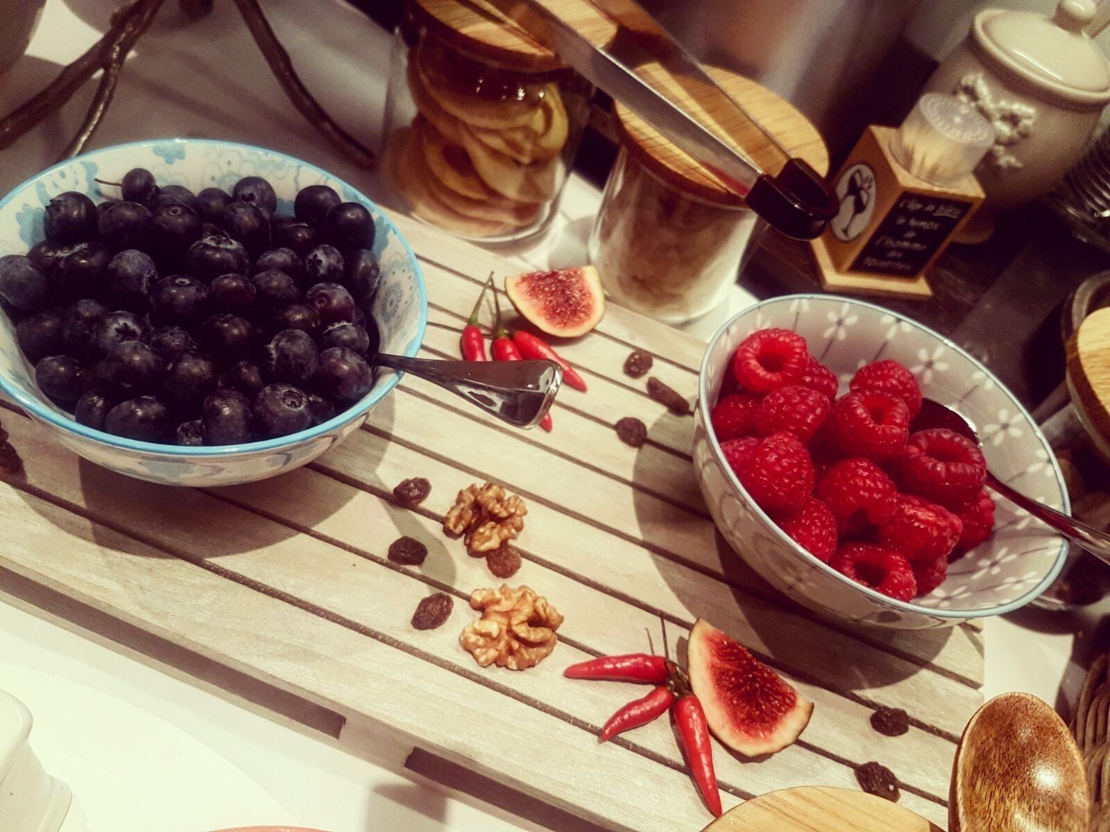 A wooden table with bowls of blueberries and raspberries, a knife, and some figs and walnuts.
