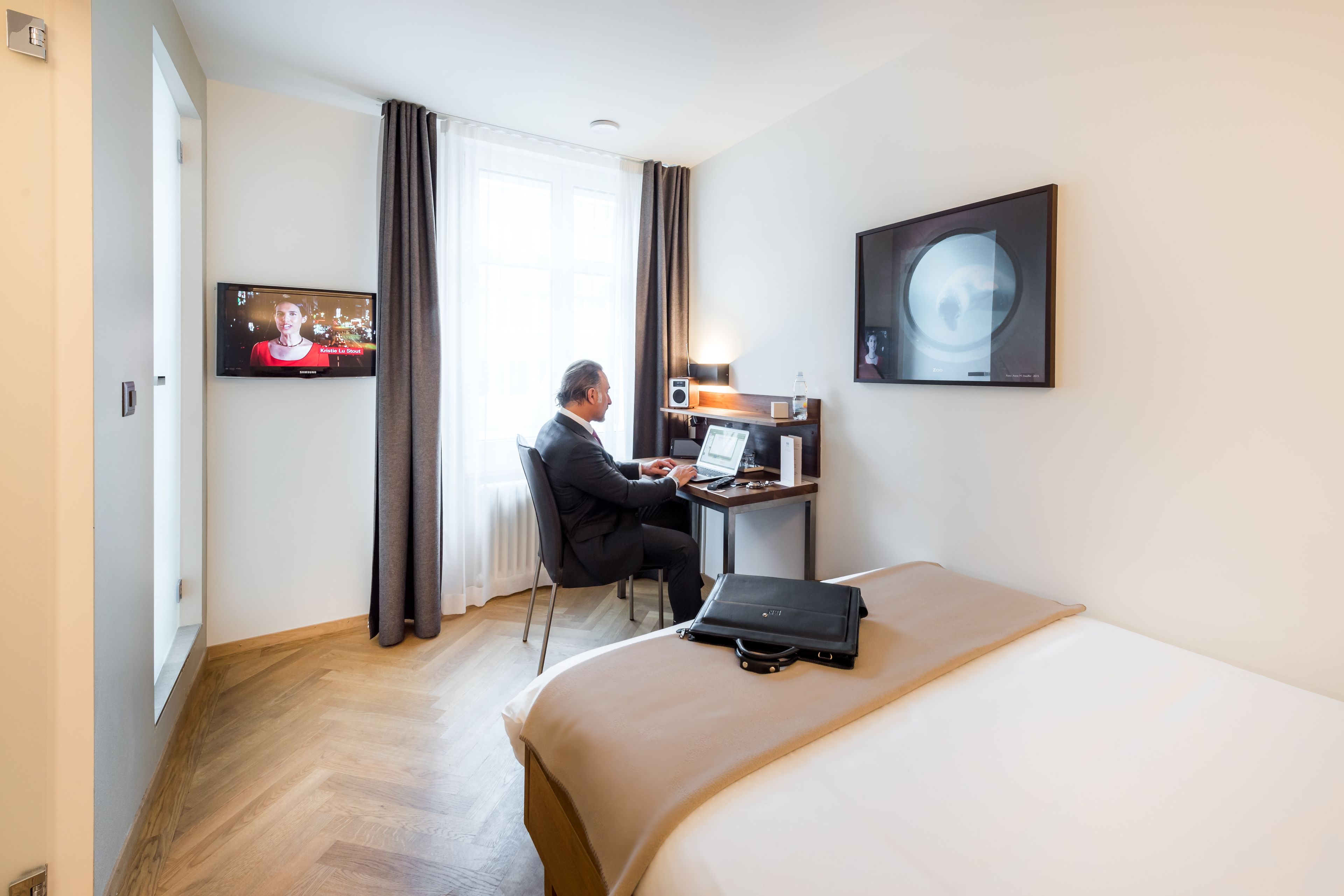 Habitación de hotel con cama, escritorio con ordenador portátil, televisor y un cuadro en la pared.