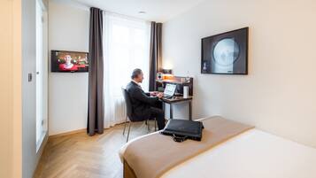 Habitación de hotel con cama, escritorio con ordenador portátil, televisor y un cuadro en la pared.